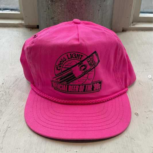 Front view of a vibrant hot pink Coors Light hat featuring the iconic 'Official Beer of the '90s' slogan in bold letters.